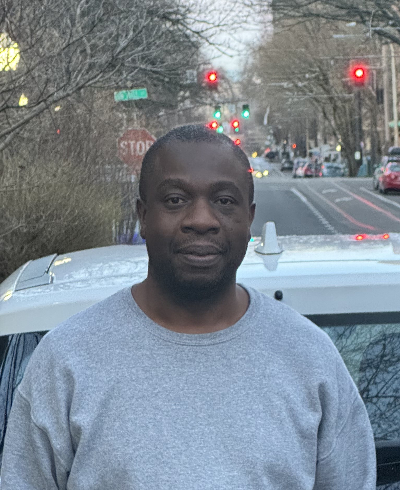 Aaron Mbwirire, a black man with black hair, standing in front of a street in Portland. 